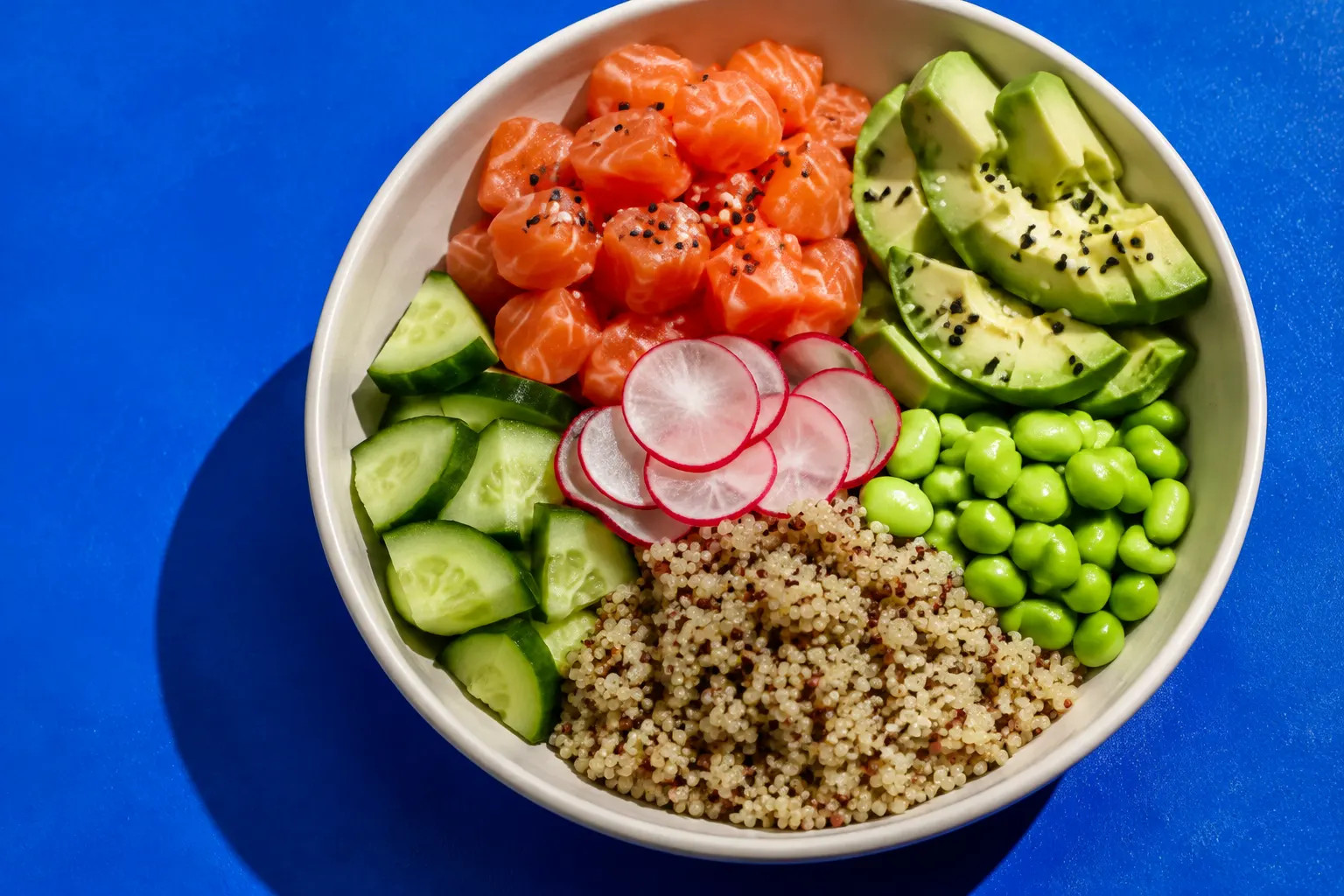 Frische Bowl mit Lachs, Avocado, Quinoa und Gemüse auf blauem Untergrund